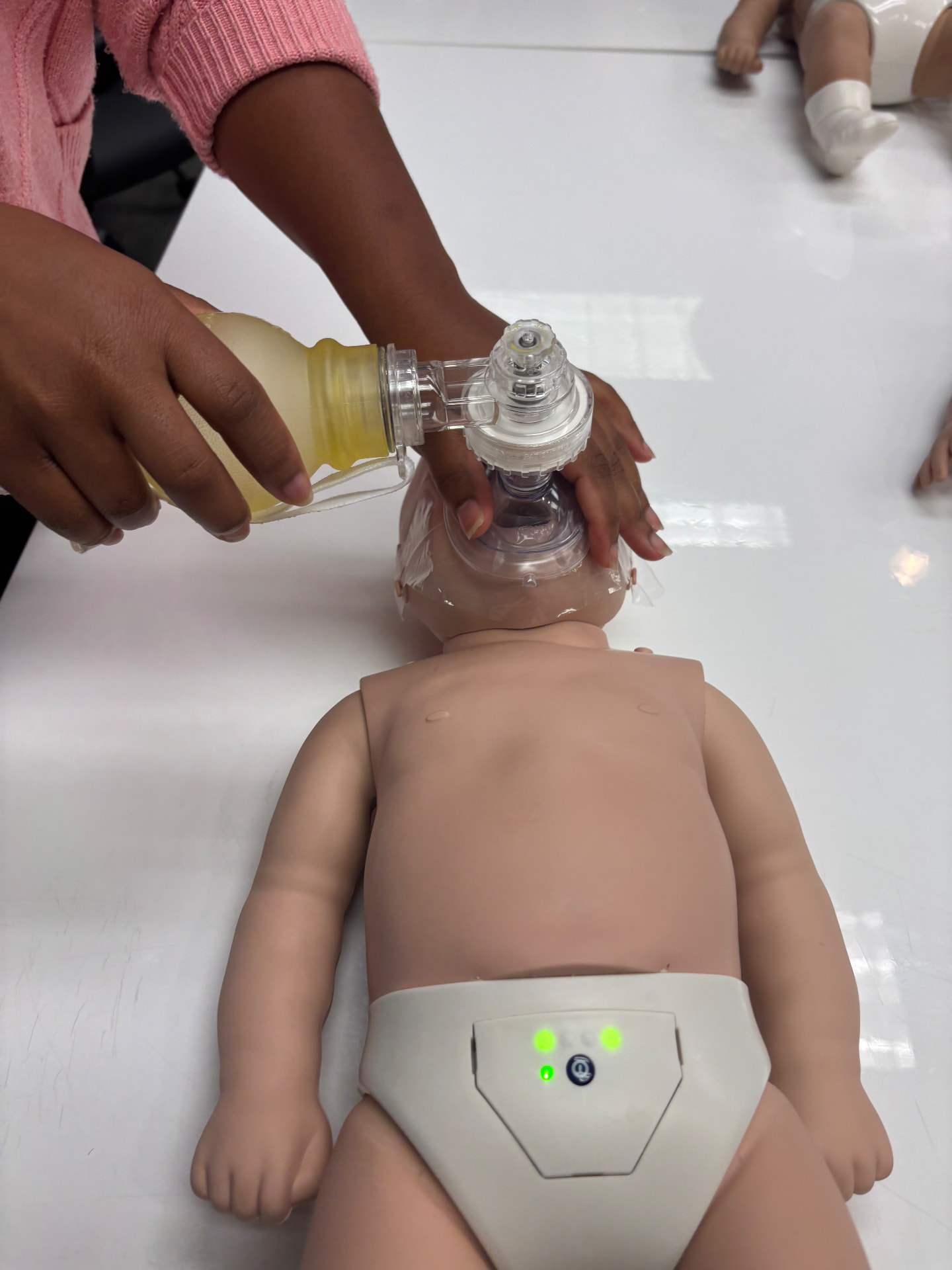 Mya practicing infant CPR with a bag valve mask on a training manikin during her certification class