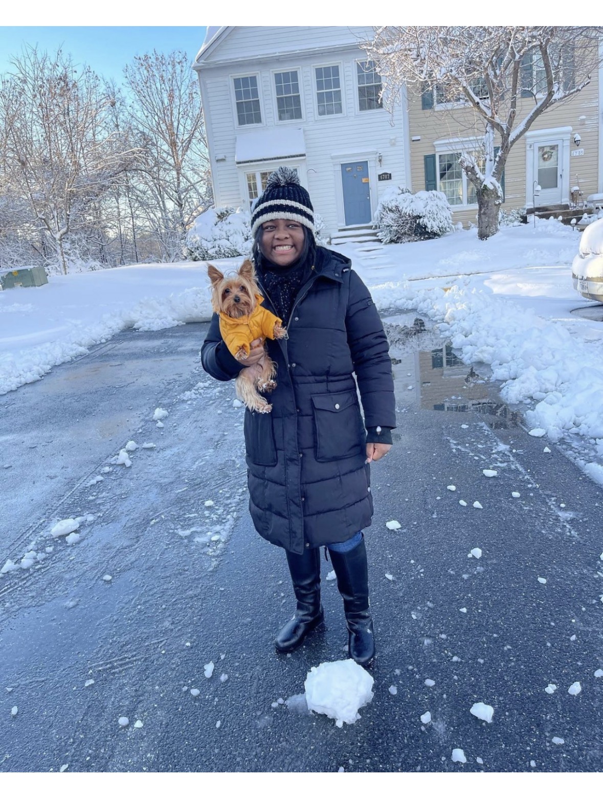 Mya holding a small Yorkie in a winter coat outside on a snowy day